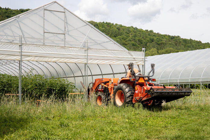 A farmer drives a tractor inside a high tunnel.